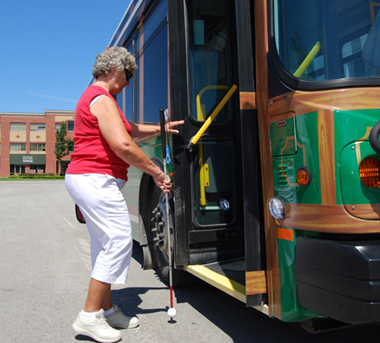 Woman with vision loss using a white cane to guide her onto a bus.
