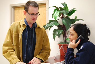 Marc with a female employee in a business setting, who is on the telephone.