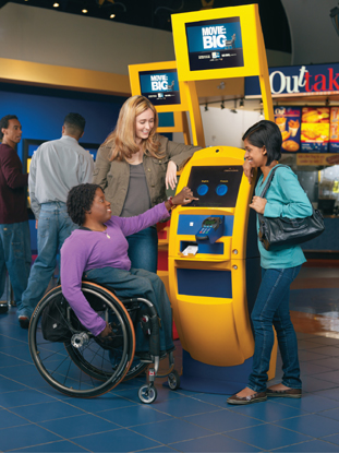 Three young woman, one in a wheelchair, purchasing movie tickets from an automated kiosk.
