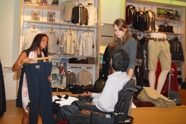 Man in a wheelchair with young woman - support person - being shown merchandise by an employee in a clothing store.