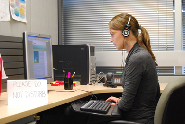 Young woman at a desk using the computer, wearing headphones.